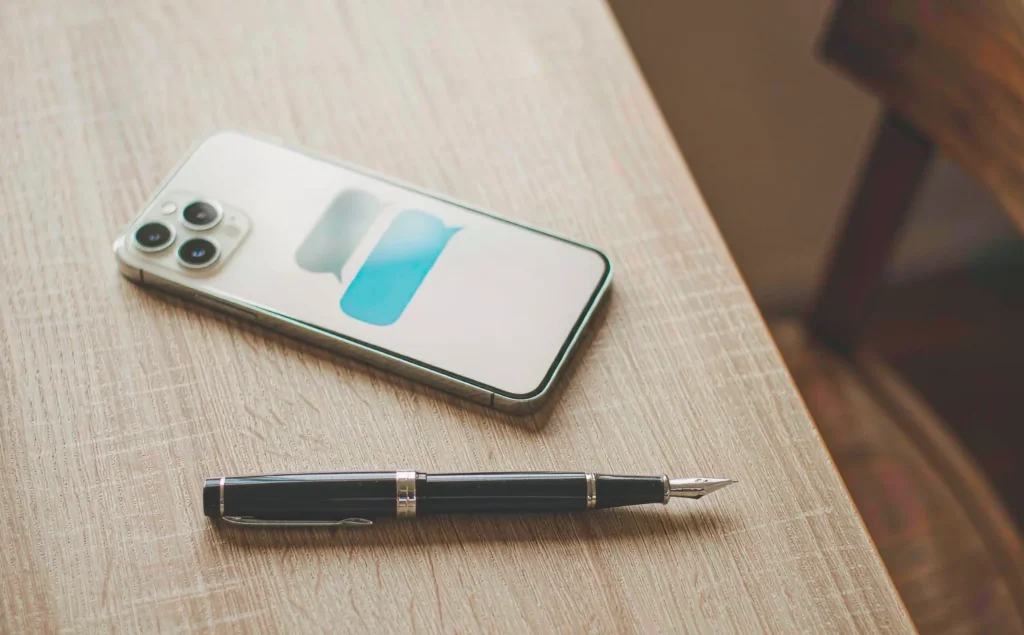 Penna stilografica e smartphone con bolle di messaggi sfocate affiancati su una scrivania di legno