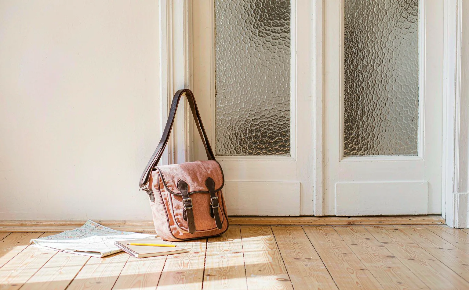 Borsa da viaggio in tela accanto a una mappa piegata e a un taccuino, vicino alla porta di casa