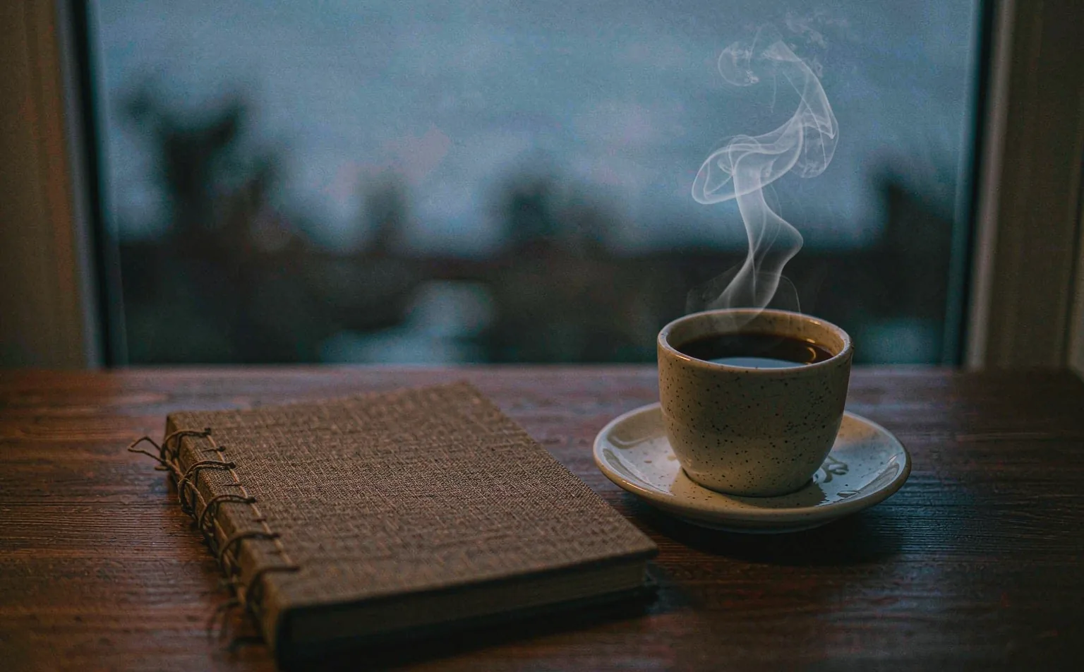 Un tavolo di prima mattina con un quaderno e una tazza di caffè: la lettura del giorno comincia presto